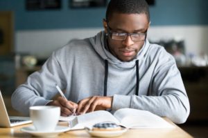 OLSAT 8 - Focused millennial African American student making notes while studying in cafe